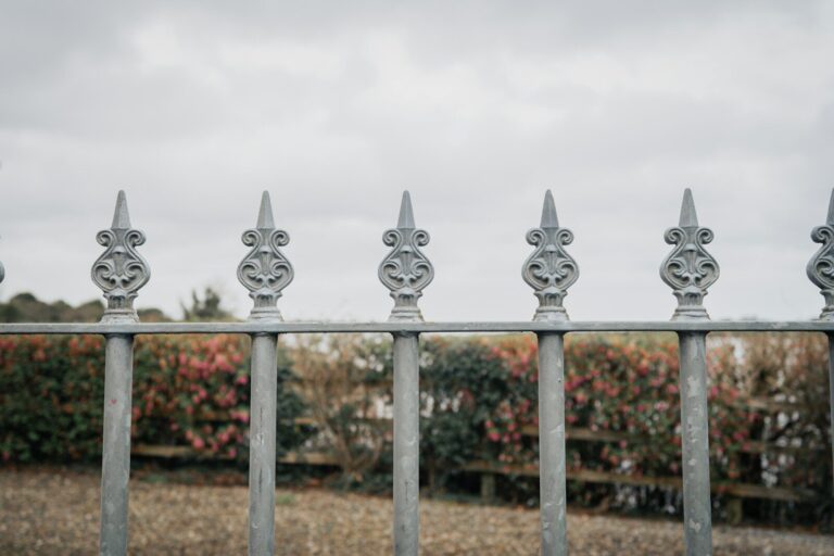 Ornate metal fence with decorative finials against cloudy sky